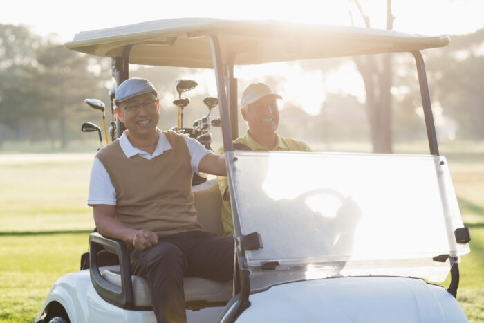 Happy golfer friends sitting in golf buggy on sunny day